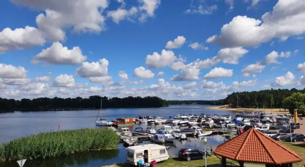 Letni dzień nad jeziorem w Koninie. Port pełen łodzi, przy brzegu kampery i zielona trawa.