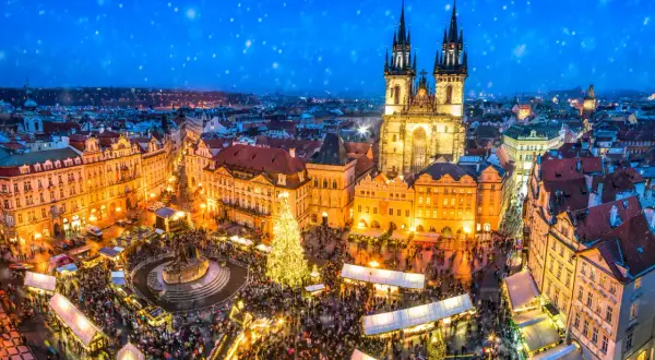 Tłoczny jarmark bożonarodzeniowy na Rynku Staromiejskim w Pradze. Śnieg prószy nad oświetloną choinką i tłumami ludzi. To magiczne święta w Czechach.
