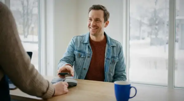 Uśmiechnięty mężczyzna płaci telefonem w Szwecji. Choć nie można tam płacić euro, transakcja przebiega sprawnie.