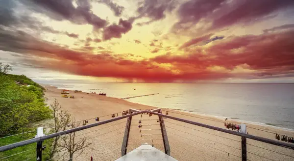 Spektakularny zachód słońca nad morzem, z ognistymi chmurami i łodziami na piaszczystej plaży. Pogorzelica w całej okazałości.