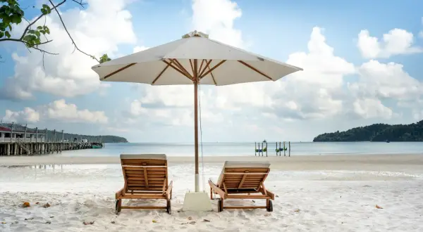 Dwie leżaki pod parasolem na piaszczystej plaży. Idealna pogoda na Korfu w czerwcu, błękitne niebo z chmurami, spokojne morze.