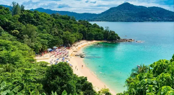 Rajska plaża Kata Beach z turkusową wodą, zielonymi wzgórzami i mnóstwem kolorowych parasoli.