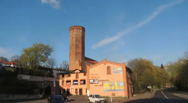 Wieża w Kamieniu Krajeńskim góruje nad budynkami z pizzerią i sklepem.