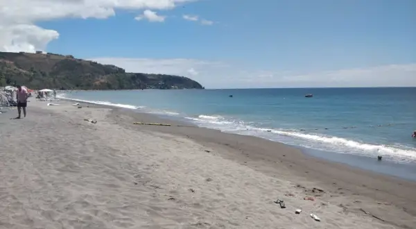 Piękna plaża na wyspie Dominika. Ciemny piasek, turkusowe morze i zielone wzgórza w tle. Idealne miejsce na relaks.