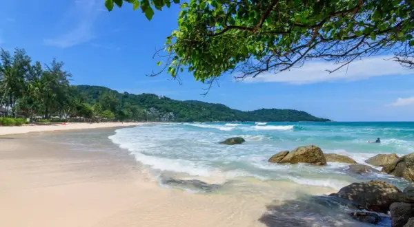 Piękna plaża Kata Beach Phuket z turkusową wodą, falami i zielonymi wzgórzami w tle. Idealne miejsce na relaks.