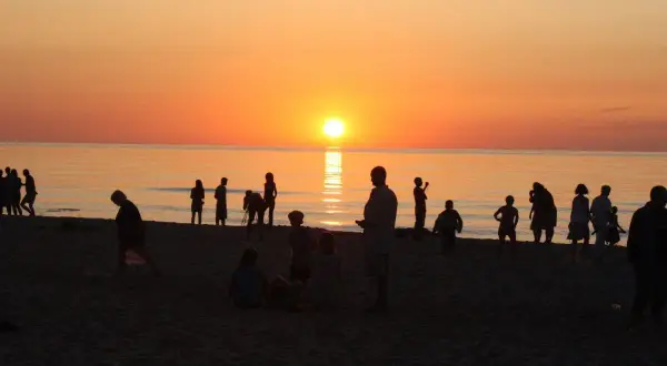 Ludzie na plaży podziwiają piękny zachód słońca w Sarbinowie. Słońce odbija się w spokojnym morzu, tworząc złocistą poświatę.