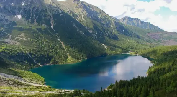 Malowniczy szlak na Morskie Oko prowadzi przez gęsty las do turkusowego jeziora otoczonego skalistymi szczytami Tatr.