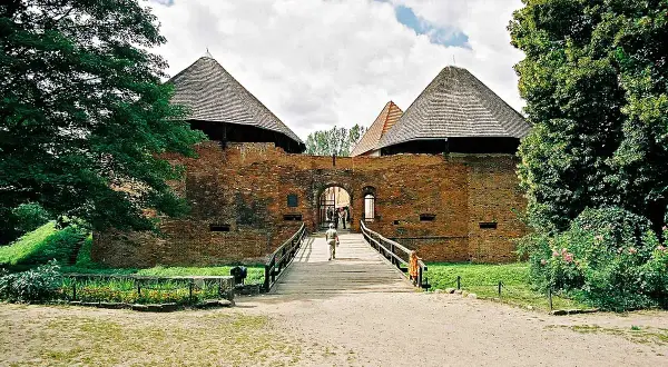 Kamienny zamek międzyrzecz z drewnianym mostem prowadzącym do bramy. Dwie okrągłe wieże z charakterystycznymi dachami.