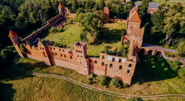 Ruiny zamku w Szymbarku, otoczone zielenią, z charakterystycznymi ceglanymi murami i wieżami.