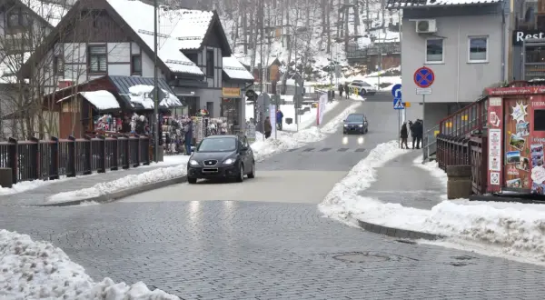 Zimowy deptak w Szklarskiej Porębie, z samochodami na ulicy i sklepikami po bokach.