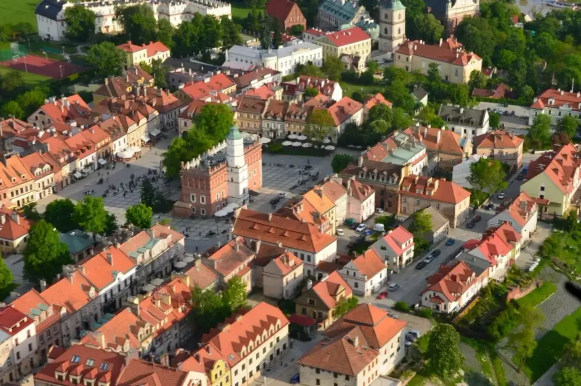 Sandomierz stare miasto z lotu ptaka. Rynek z ratuszem i kamienicami o czerwonych dachach, otoczony zielenią.