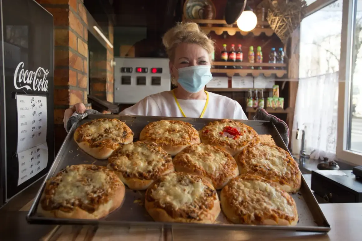 Uśmiechnięta sprzedawczyni w maseczce prezentuje tacę z zapiekanymi pizzami. To może być najstarsza pizzeria w Polsce, gdzie tradycja spotyka się z nowoczesnością.
