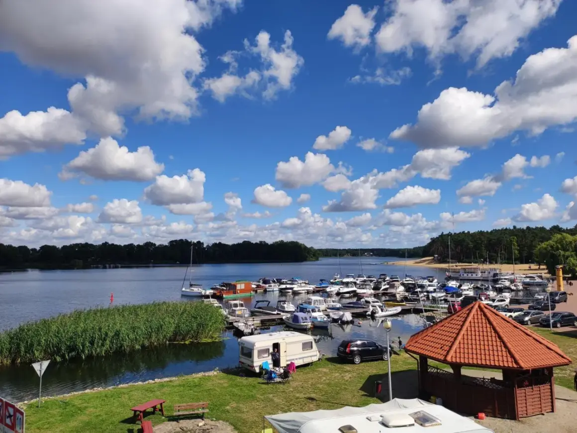Letni dzień nad jeziorem w Koninie. Port pełen łodzi, przy brzegu kampery i zielona trawa.