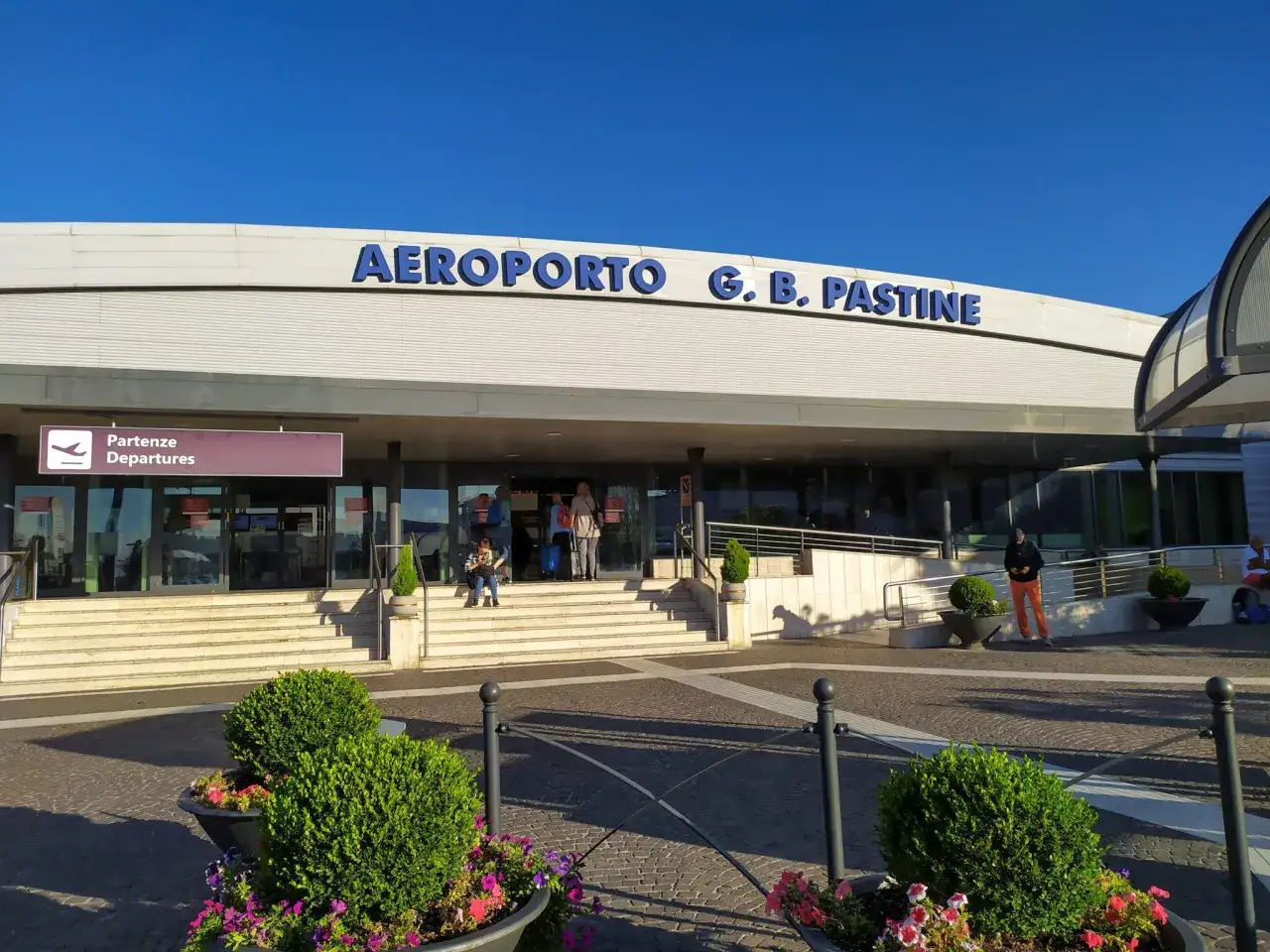 Wejście do Aeroportu G.B. Pastine w Rzymie Ciampino. Słoneczny dzień, ludzie czekają na odloty.
