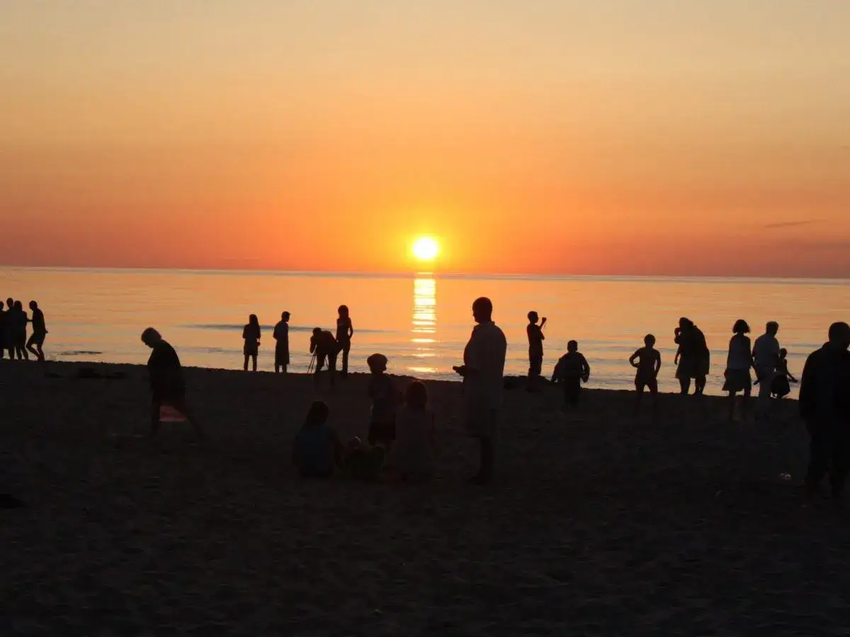 Ludzie na plaży podziwiają piękny zachód słońca w Sarbinowie. Słońce odbija się w spokojnym morzu, tworząc złocistą poświatę.