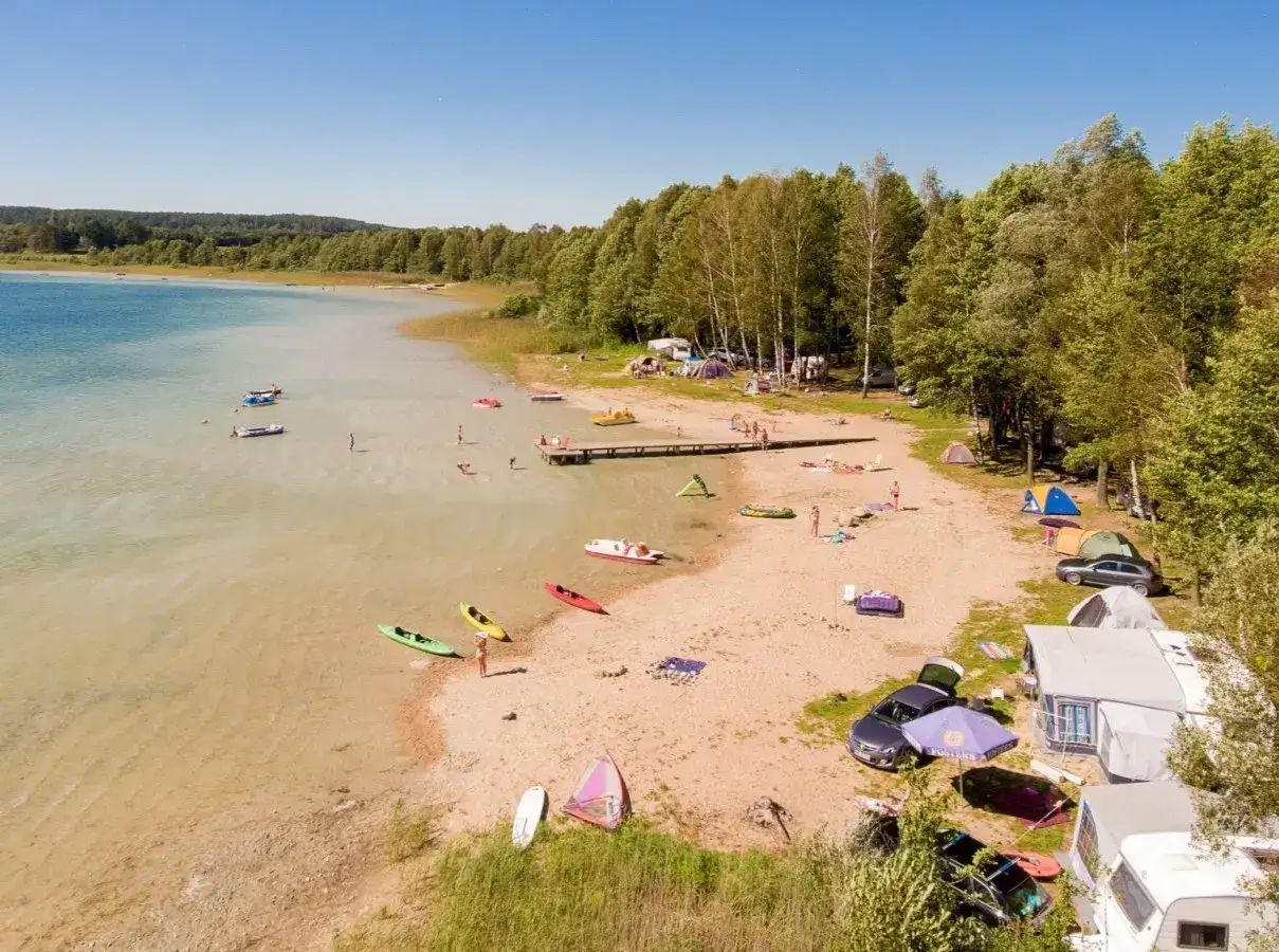 Plaża nad jeziorem Świętajno tętni życiem. Ludzie pływają, opalają się, a na piasku rozstawiono namioty i kampery.