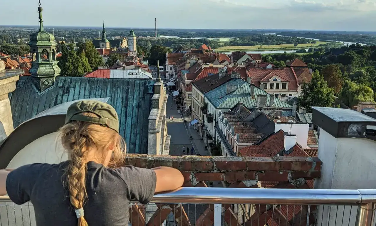Dziewczynka z warkoczem podziwia panoramę sandomierz stare miasto z wieży. W dole urokliwa uliczka i dachy kamienic.