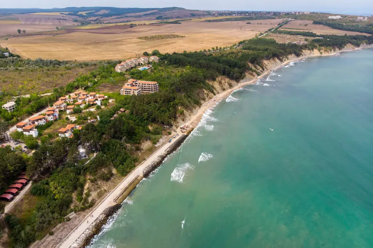 Widok z lotu ptaka na wybrzeże z hotelami i plażą. W oddali pola uprawne, a na morzu fale. Obzor atrakcje czekają!