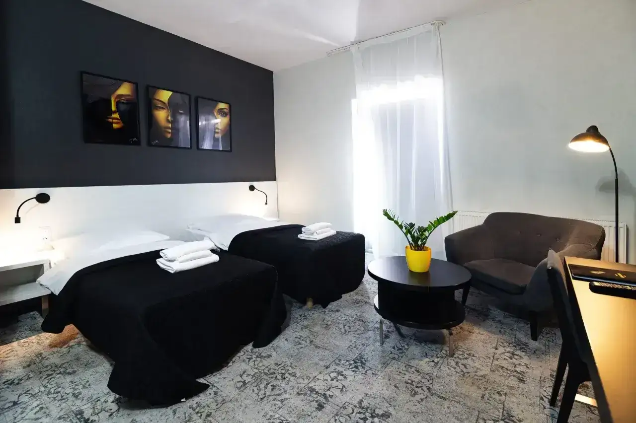 Nowoczesny pokój hotelowy z dwoma łóżkami, czarnymi narzutami i grafikami na ścianie. Idealny na komfortową dobę hotelową.