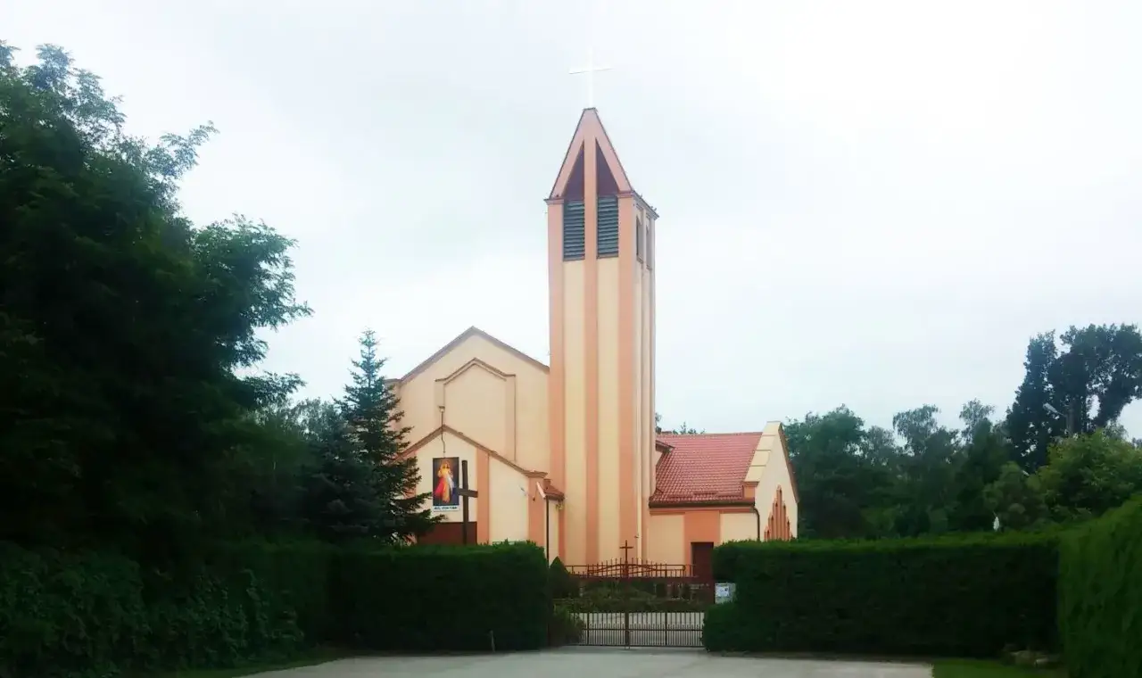 Kościół w Andrespolu z wieżą i krzyżem, otoczony zielenią.