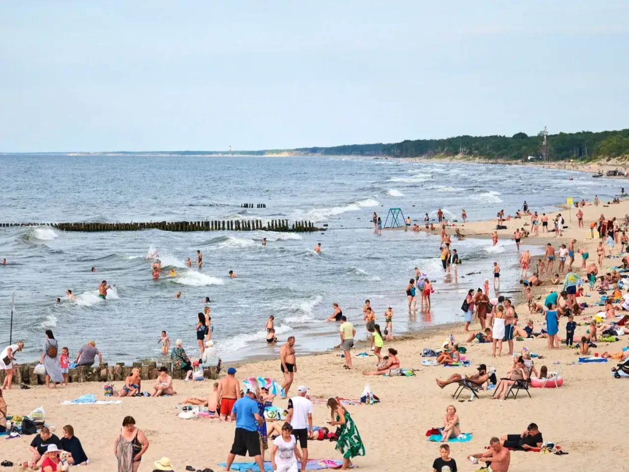 Tłum ludzi na plaży cieszy się piękną pogodą nad Bałtykiem. Kąpiel w morzu i opalanie się na piasku.