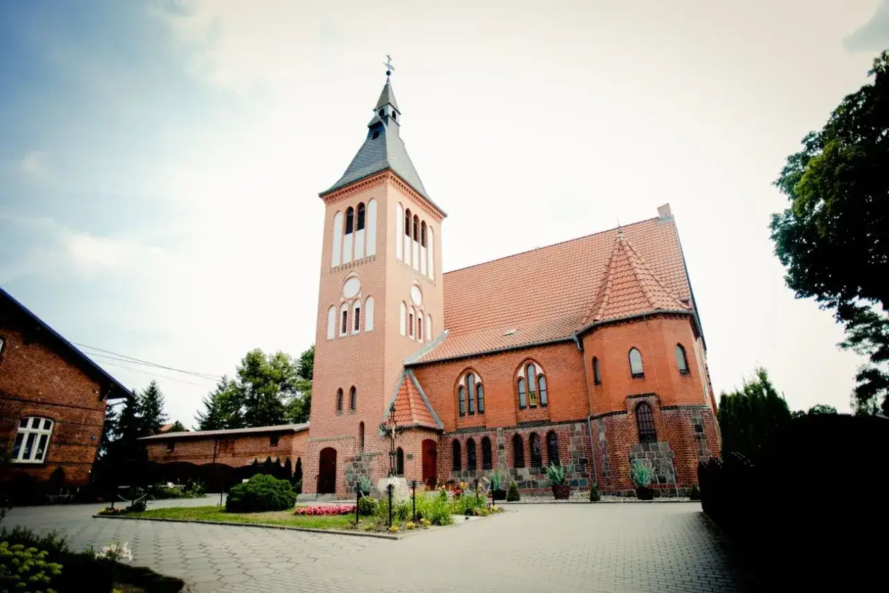 Kościół w Swarożynie, ceglana budowla z wieżą i czerwonym dachem, otoczona zielenią.