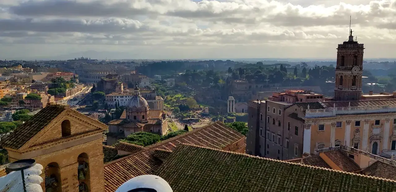 Widok na Rzym z daleka, gdzie jest koloseum, widać też Forum Romanum i wieżę z zegarem.