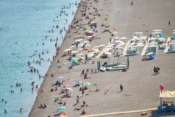Tłum ludzi odpoczywa na kamienistej plaży w Finike, kąpiąc się w morzu i opalając pod parasolami.