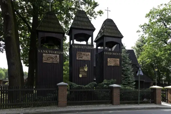 Trzy drewniane dzwonnice przed kościołem w Jankowicach. Na jednej z nich widnieje napis "Sanktuarium Najświętszego Sakramentu".