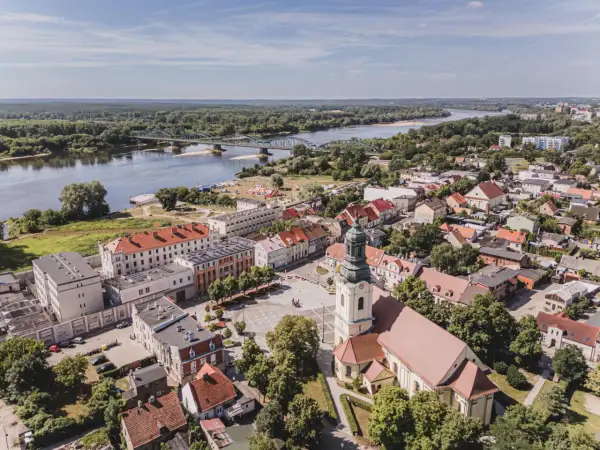 Widok z lotu ptaka na miasto z rzeką i mostem. W centrum plac z kościołem, a w oddali widać zabudowania i las. Na jednym z budynków widoczny napis "Fordon".