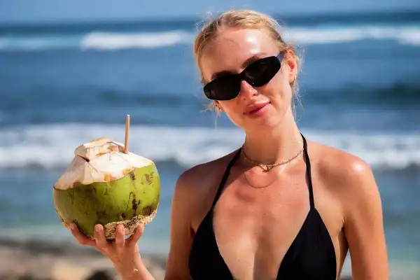 Kobieta w czarnym bikini trzyma kokosa na plaży. Idealne wakacje na Bali z orzeźwiającym napojem.