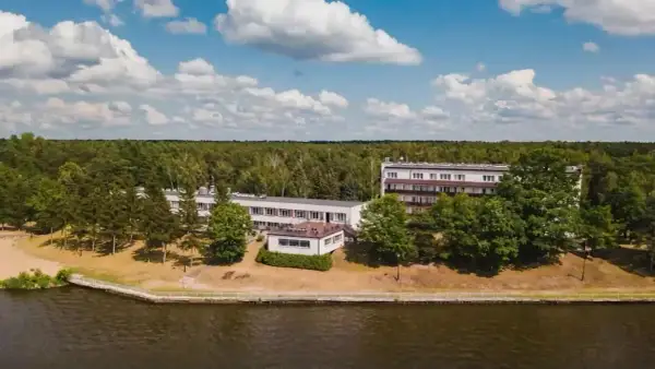 Budynki hotelowe w Ryni nad jeziorem, otoczone lasem i zielenią.