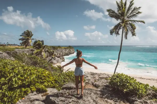 Kobieta z rozłożonymi rękami podziwia turkusowe morze i palmę. Idealne Barbados wakacje.