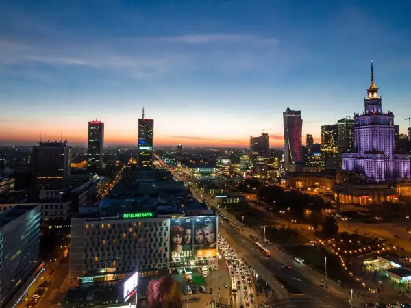 Wieczorna panorama Warszawy, największego miasta w Polsce. Widać Pałac Kultury i Nauki, nowoczesne wieżowce i ruchliwe ulice.