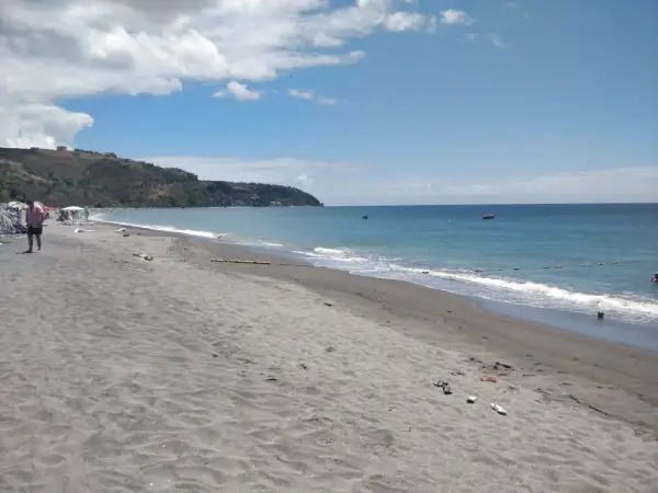 Piękna plaża na wyspie Dominika. Ciemny piasek, turkusowe morze i zielone wzgórza w tle. Idealne miejsce na relaks.
