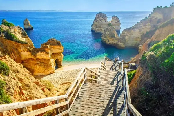 Malownicze klify i turkusowa woda, idealne na portugalia wakacje. Drewniane schody prowadzą na piaszczystą plażę.